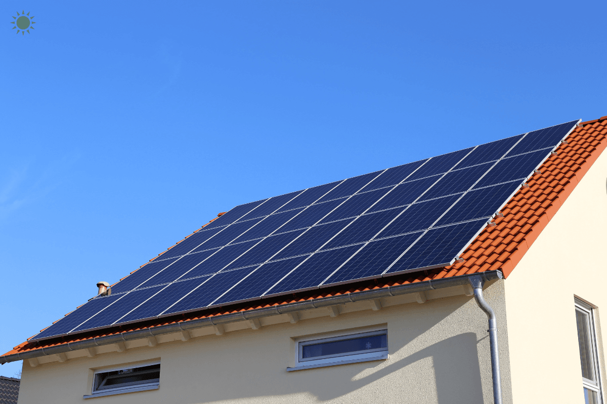 Rooftop solar panels installed on a red-tiled residential home under a clear blue sky, with panels covering most of the sloped roof.