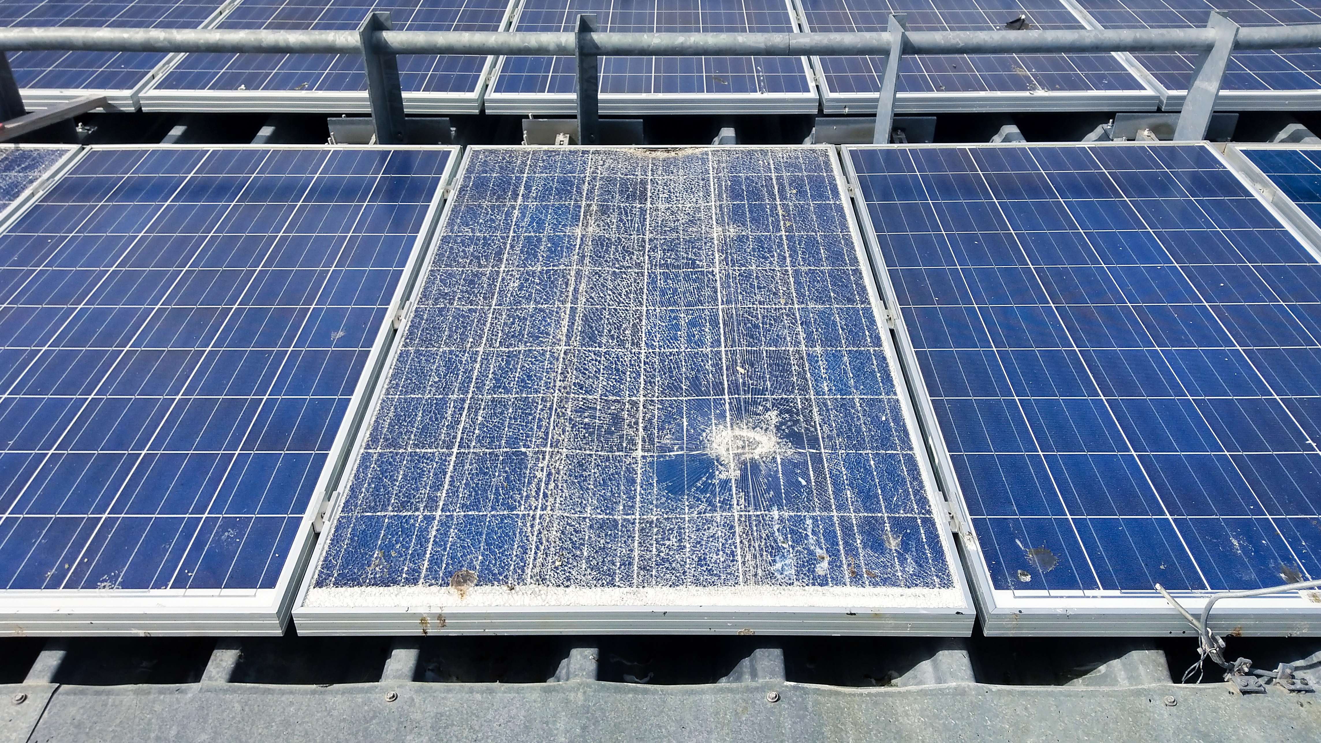 Damaged solar panel showing significant wear and deterioration between two well-maintained panels